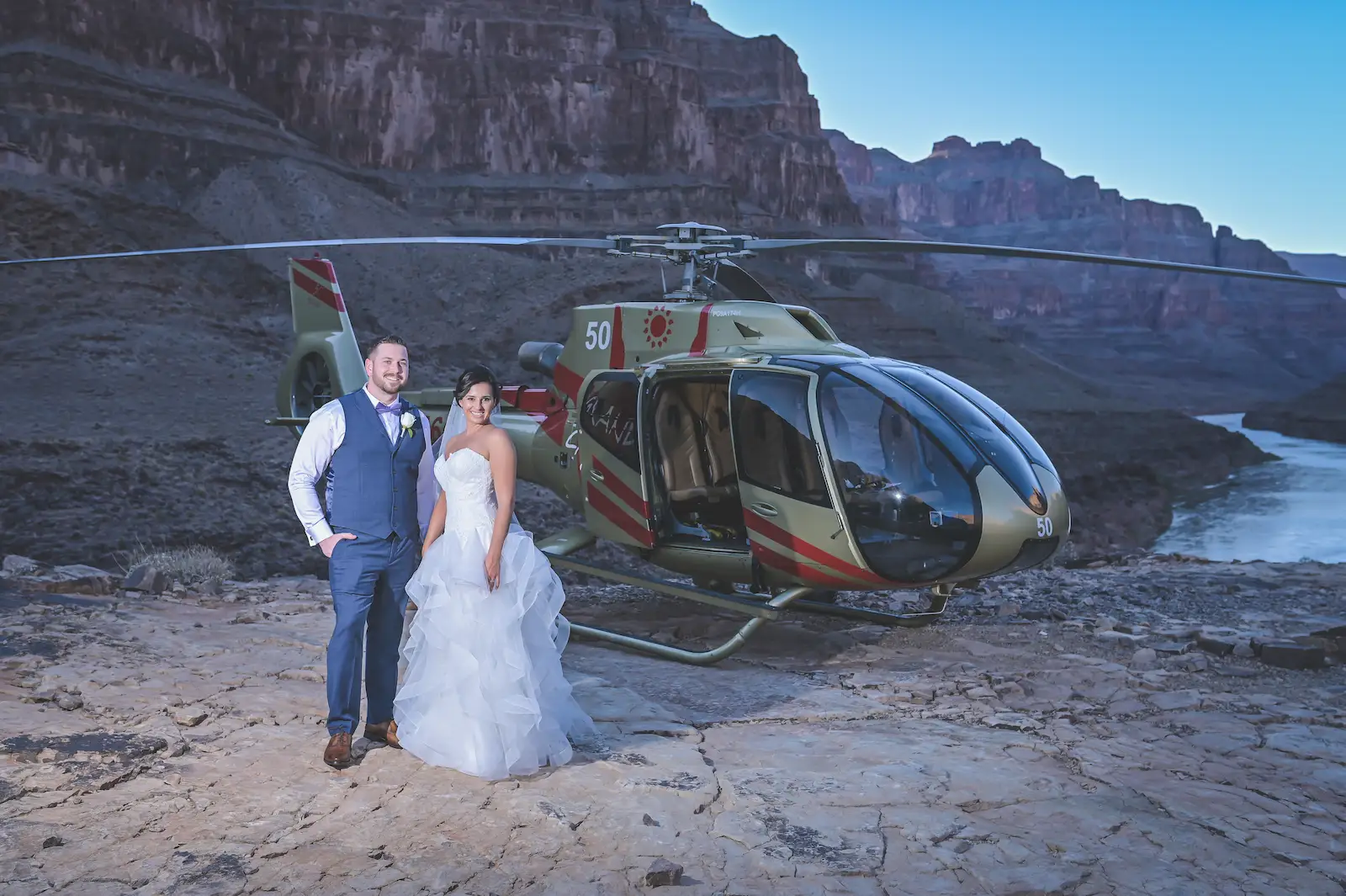 Bride and groom posing beside a Grand Canyon helicopter at dusk at the bottom of the canyon