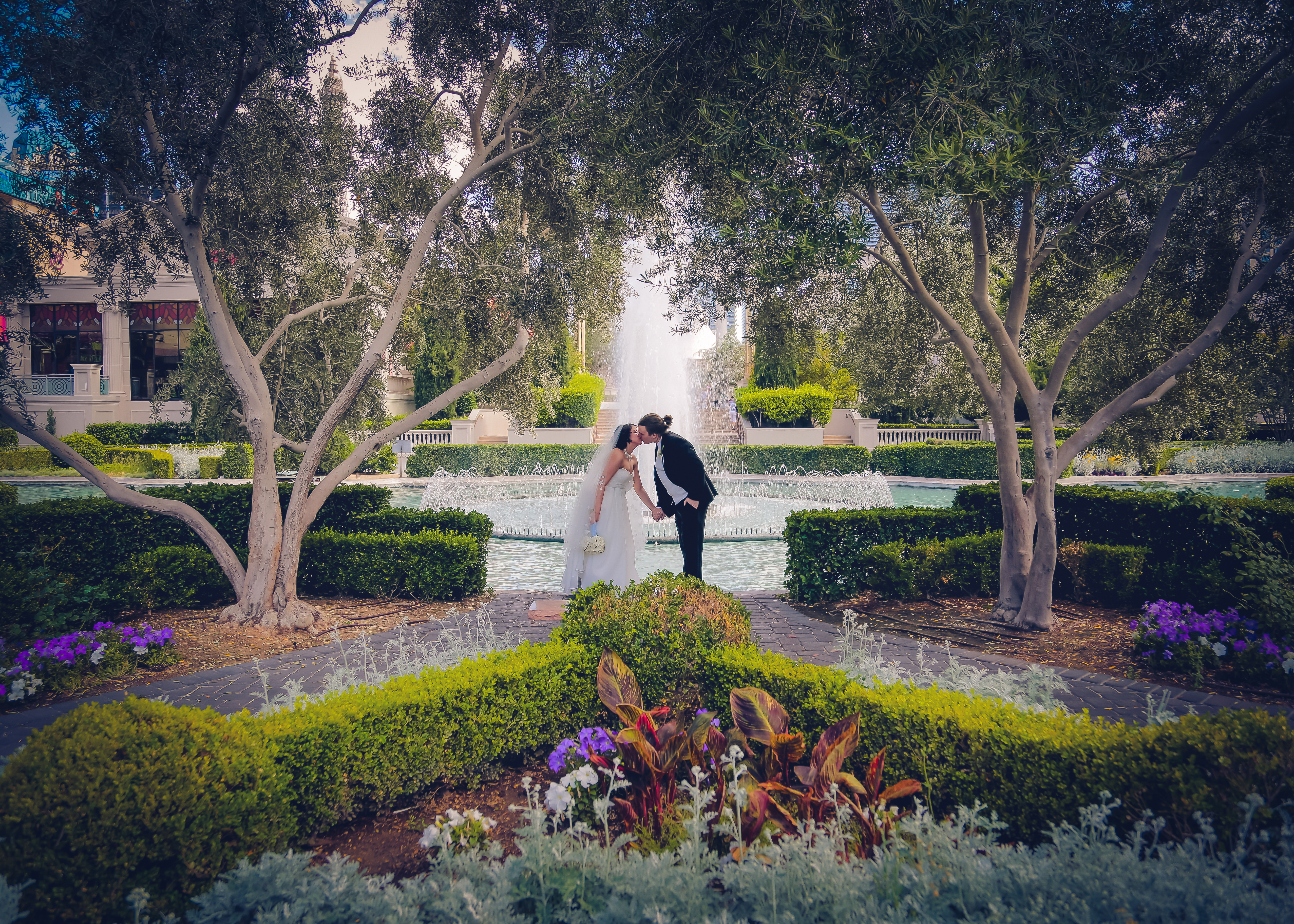 Husband and wife kissing in front of a garden fountain 