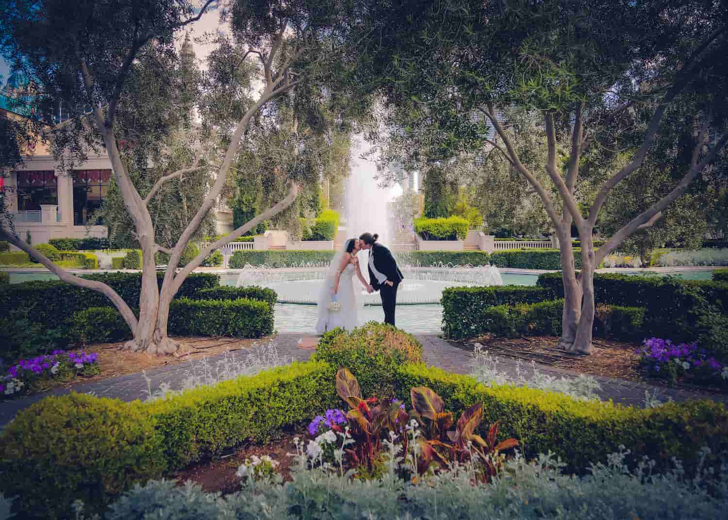 Husband and wife kissing in front of a garden fountain 